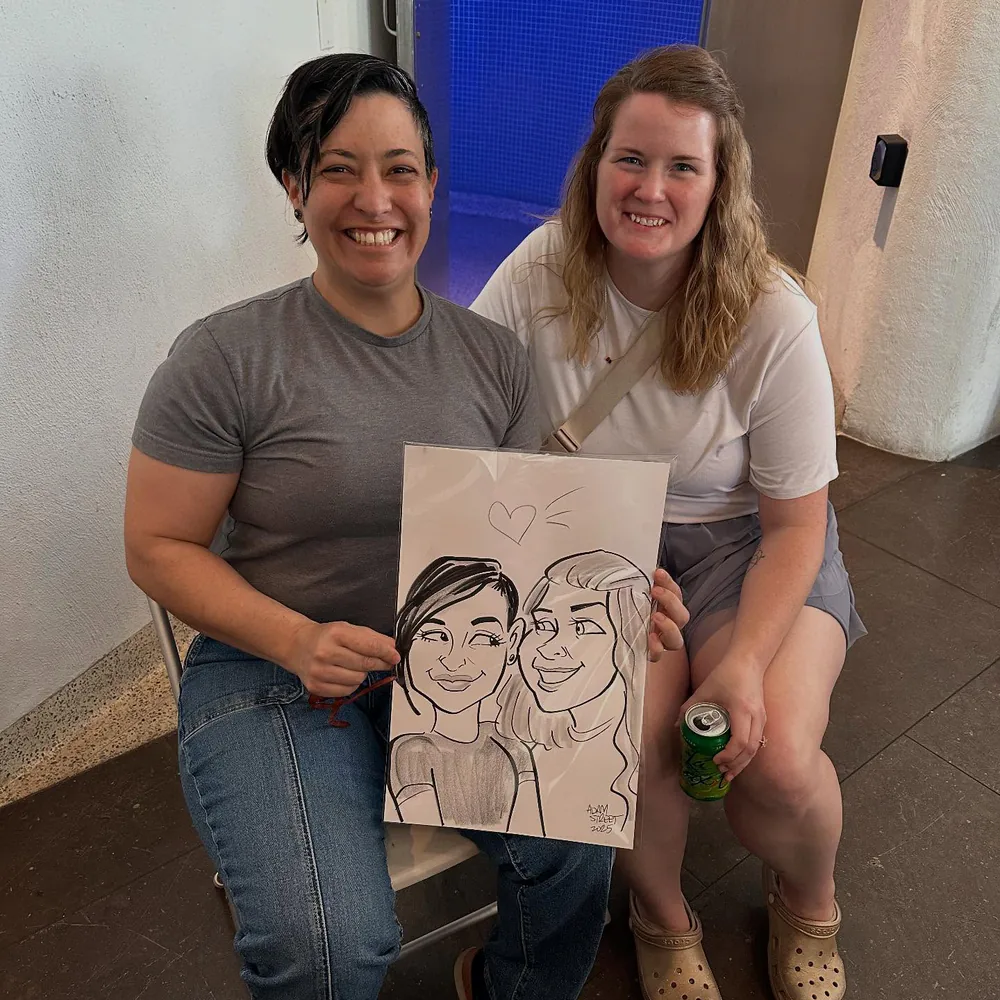 Two smiling guests seated together holding their Adam Street caricature